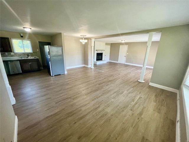 unfurnished living room featuring a sink, a brick fireplace, wood finished floors, and baseboards