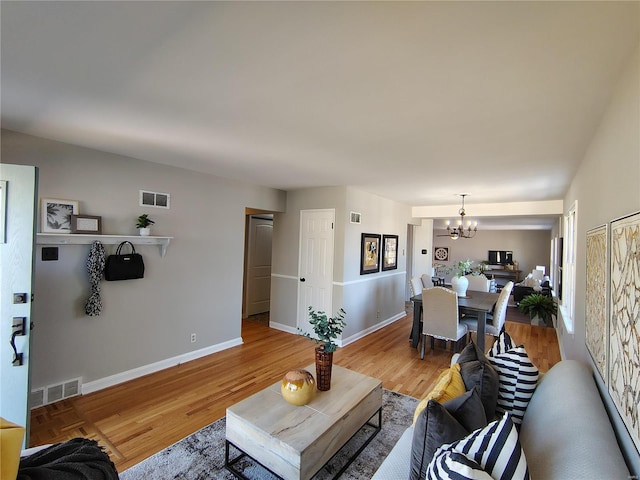 living area featuring visible vents, baseboards, an inviting chandelier, and light wood finished floors