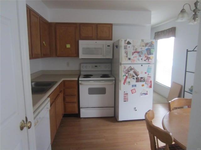 kitchen featuring white appliances, brown cabinets, light countertops, light wood-type flooring, and a sink