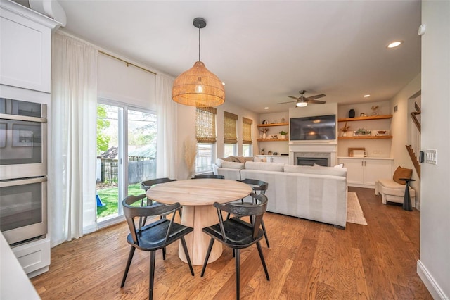 dining space with ceiling fan, a fireplace, recessed lighting, and light wood-style flooring