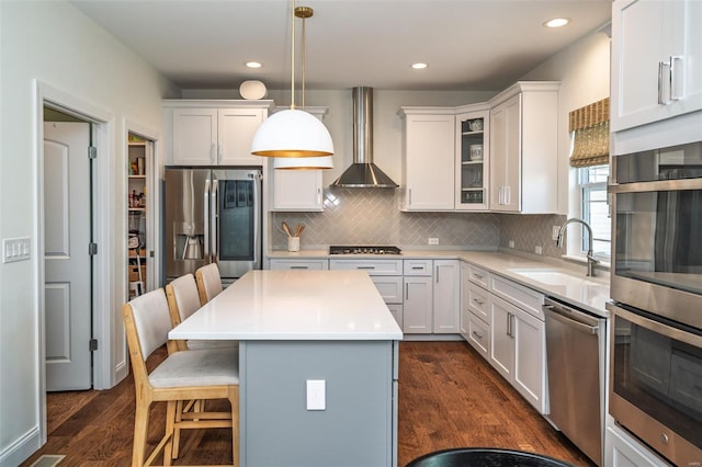 kitchen with wall chimney range hood, a kitchen breakfast bar, dark wood-style flooring, a sink, and stainless steel appliances
