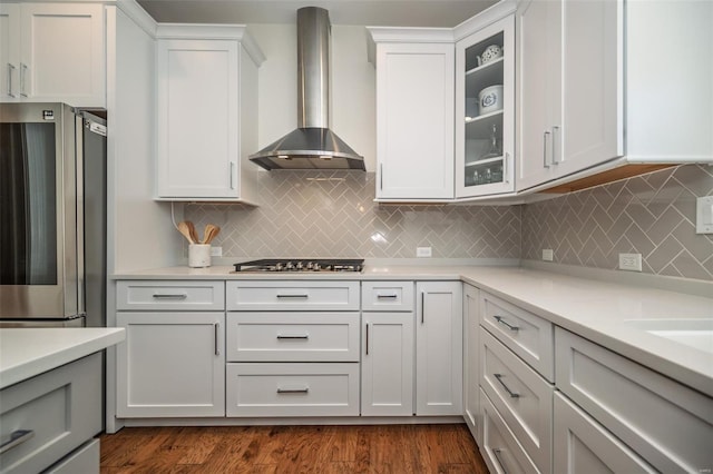 kitchen with wall chimney range hood, appliances with stainless steel finishes, light countertops, glass insert cabinets, and white cabinetry
