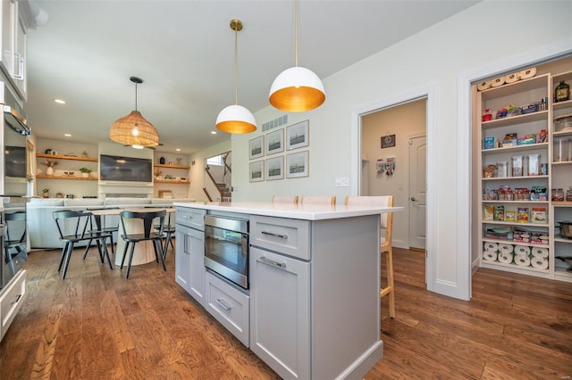 kitchen with hanging light fixtures, light countertops, a kitchen breakfast bar, dark wood finished floors, and gray cabinetry