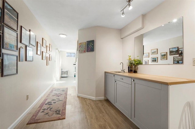 hall featuring rail lighting, light wood-type flooring, baseboards, and a sink