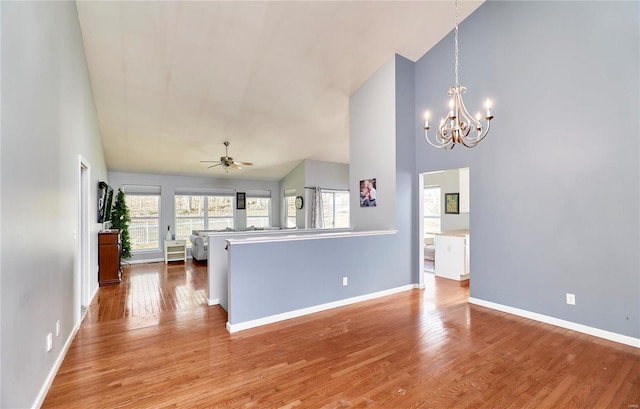 interior space with hanging light fixtures, a towering ceiling, light wood-type flooring, baseboards, and ceiling fan with notable chandelier