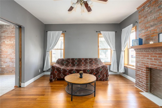 sitting room with hardwood / wood-style flooring, a brick fireplace, baseboards, and ceiling fan