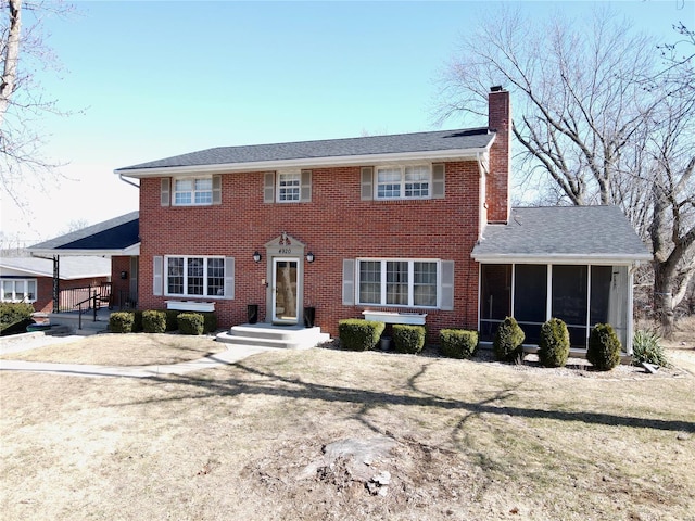 colonial inspired home featuring a sunroom, a chimney, and brick siding