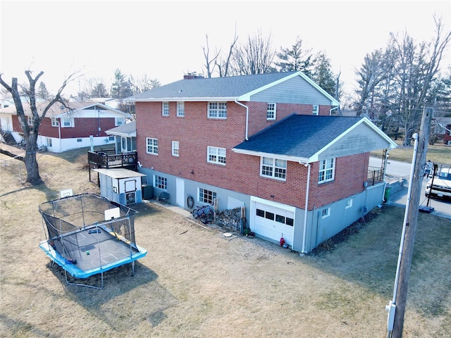 rear view of property featuring a garage, brick siding, driveway, a lawn, and a trampoline