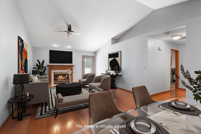 living room featuring vaulted ceiling, ceiling fan, a glass covered fireplace, and wood finished floors