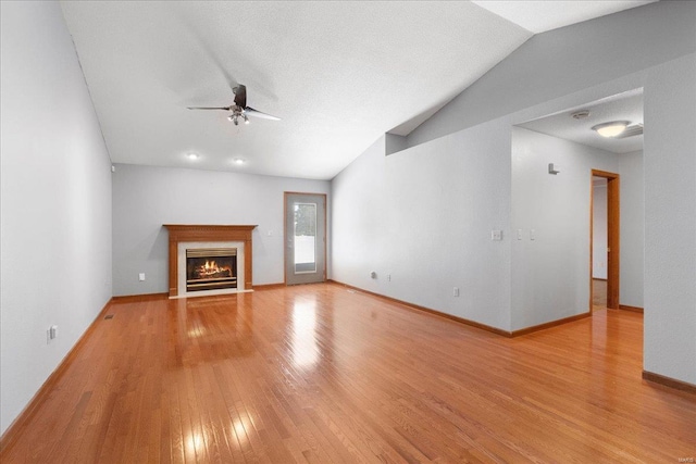 unfurnished living room featuring lofted ceiling, a fireplace with flush hearth, ceiling fan, wood finished floors, and baseboards