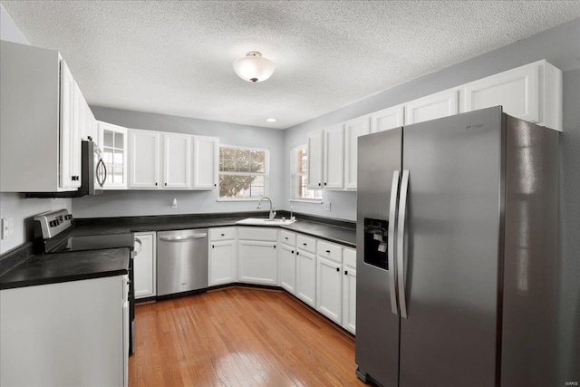 kitchen featuring stainless steel appliances, dark countertops, a sink, and light wood finished floors