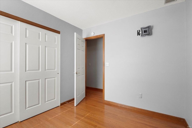 unfurnished bedroom with a textured ceiling, a closet, light wood-type flooring, and baseboards