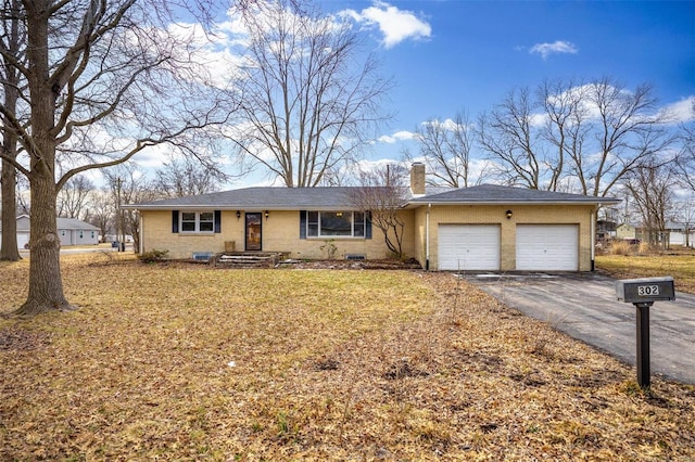 ranch-style house with aphalt driveway, an attached garage, brick siding, a chimney, and a front yard