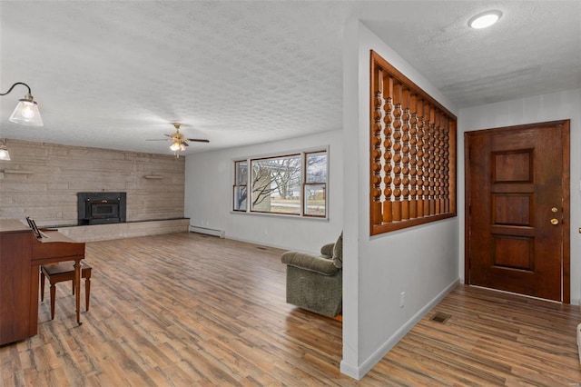 interior space featuring baseboard heating, a wood stove, a textured ceiling, wood finished floors, and baseboards