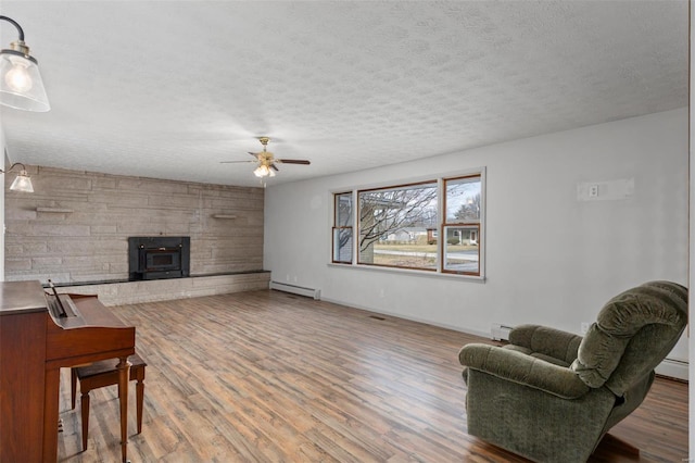 living area with a textured ceiling, a baseboard heating unit, a baseboard radiator, and wood finished floors