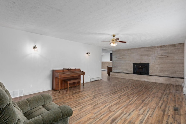 living room with a textured ceiling, visible vents, baseboard heating, and wood finished floors