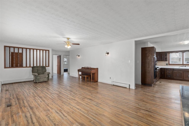 unfurnished living room with a ceiling fan, a baseboard radiator, a textured ceiling, and wood finished floors