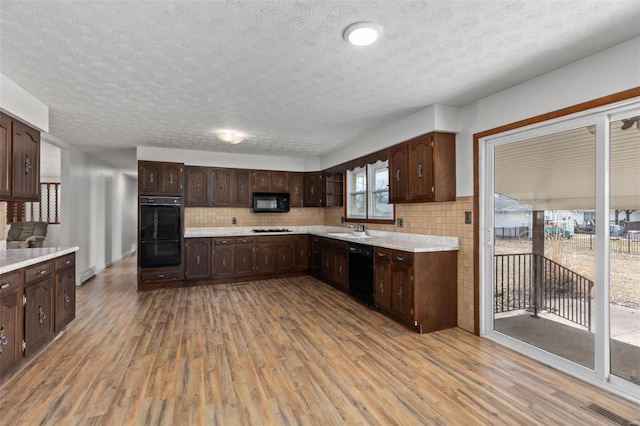 kitchen featuring light wood-style flooring, a sink, dark brown cabinets, light countertops, and black appliances