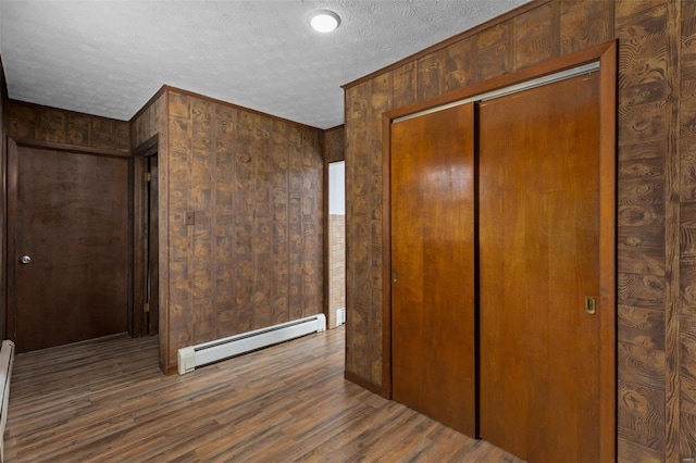 unfurnished bedroom featuring a baseboard radiator, a closet, a textured ceiling, and wood finished floors