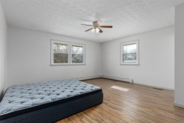 bedroom featuring a baseboard radiator, visible vents, a textured ceiling, wood finished floors, and baseboards