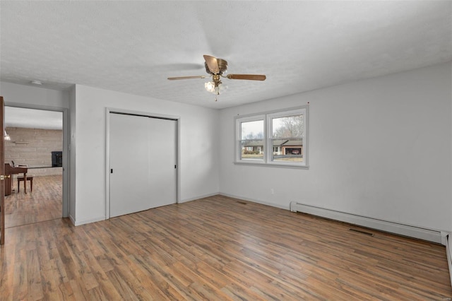 unfurnished bedroom featuring a closet, baseboard heating, a ceiling fan, a textured ceiling, and wood finished floors