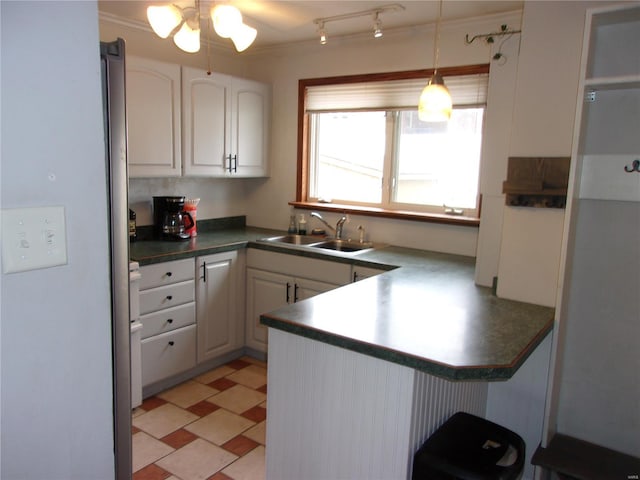 kitchen with white cabinets, dark countertops, a peninsula, light floors, and a sink