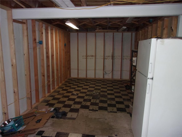 unfinished basement with tile patterned floors and freestanding refrigerator