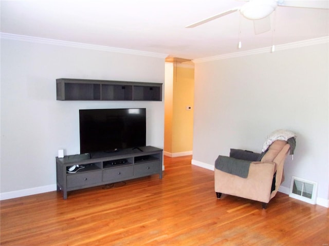 living area with baseboards, wood finished floors, visible vents, and crown molding