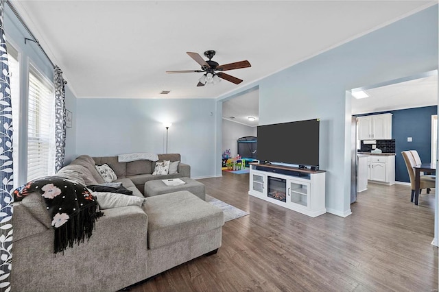 living area with dark wood-type flooring, crown molding, ceiling fan, and baseboards