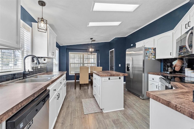 kitchen with stainless steel appliances, butcher block countertops, a kitchen island, a sink, and light wood finished floors