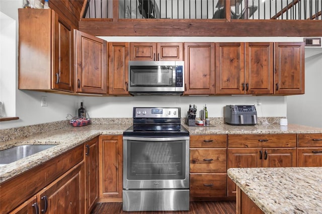 kitchen featuring appliances with stainless steel finishes, brown cabinets, dark wood-type flooring, and light stone counters