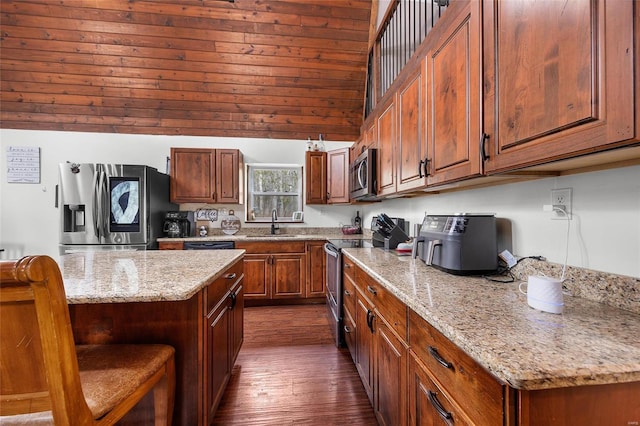 kitchen with light stone counters, dark wood-type flooring, a sink, a kitchen breakfast bar, and appliances with stainless steel finishes