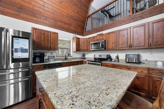 kitchen with appliances with stainless steel finishes, a center island, a sink, and light stone countertops