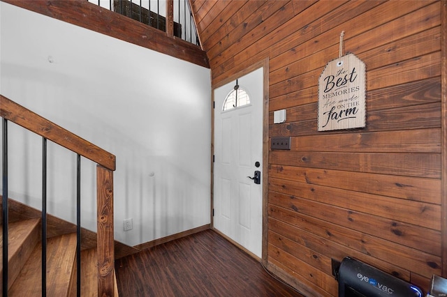 entrance foyer with dark wood-style floors, wooden walls, a high ceiling, and baseboards