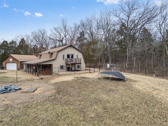 back of property featuring an attached garage, fence, a gambrel roof, a wooden deck, and a trampoline