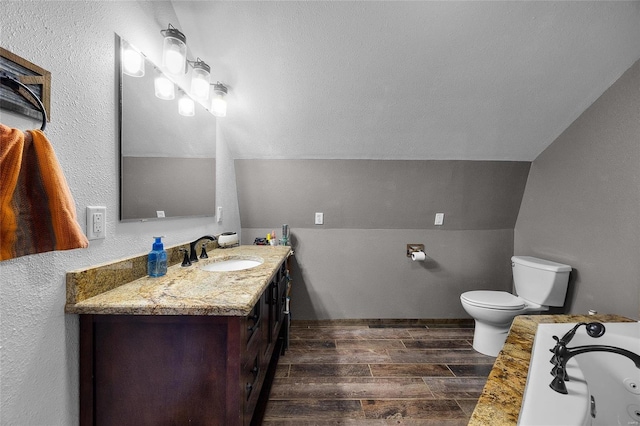 bathroom featuring toilet, wood tiled floor, vaulted ceiling, vanity, and a tub with jets