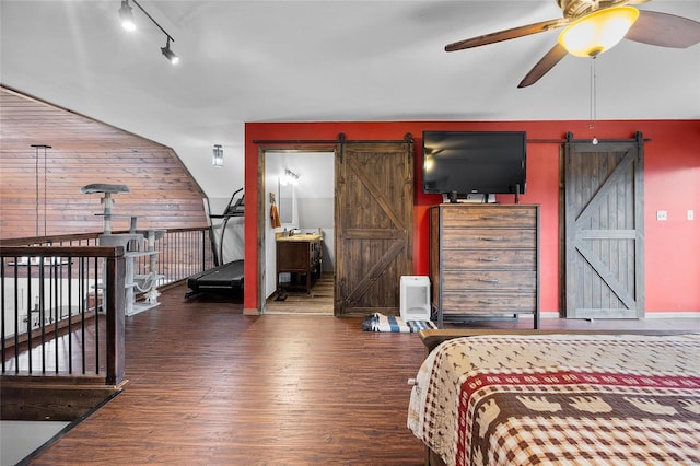 bedroom featuring wood finished floors, wooden walls, track lighting, and a barn door