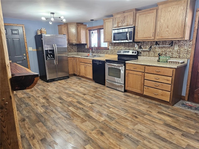 kitchen with stainless steel appliances, light countertops, backsplash, a sink, and wood finished floors