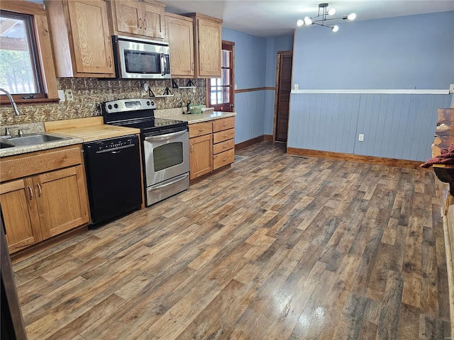 kitchen featuring stainless steel appliances, light countertops, wainscoting, a sink, and wood finished floors