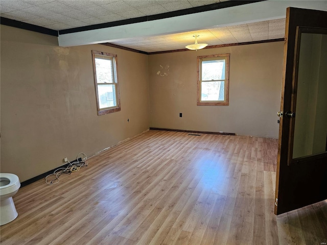 empty room with light wood-style floors, visible vents, plenty of natural light, and ornamental molding