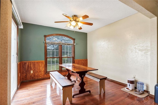 dining room with a wainscoted wall, light wood-style floors, a ceiling fan, wood walls, and a textured ceiling