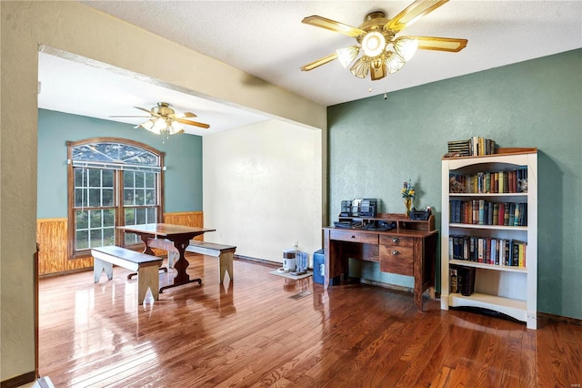 interior space with ceiling fan, wainscoting, a textured wall, and wood finished floors