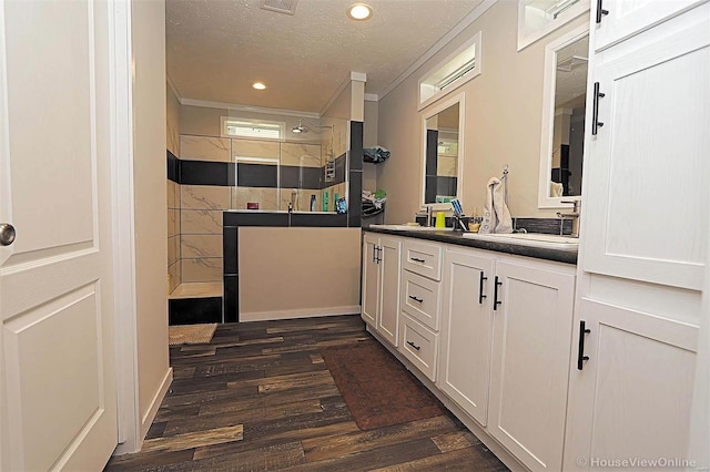 bathroom featuring crown molding, double vanity, a textured ceiling, wood finished floors, and walk in shower