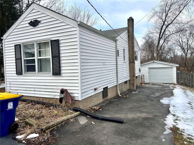 view of side of property with an outbuilding, driveway, a chimney, and a detached garage