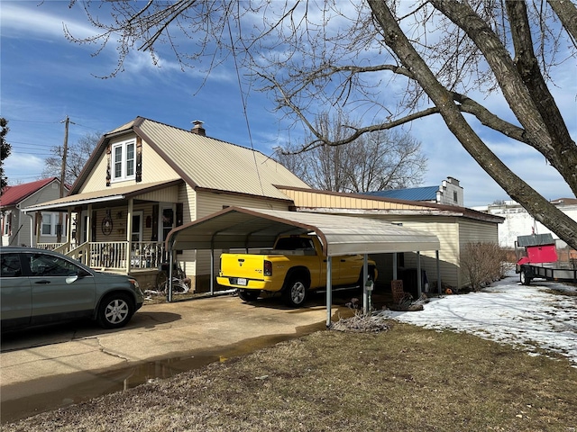 view of snowy exterior with metal roof, a chimney, a porch, and a detached carport