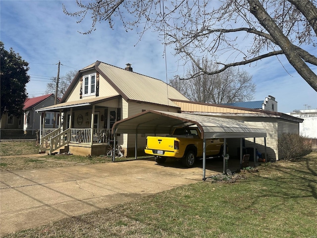 view of front of home with a front lawn, a porch, a chimney, metal roof, and driveway