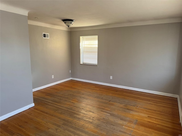 spare room featuring baseboards, visible vents, and dark wood finished floors