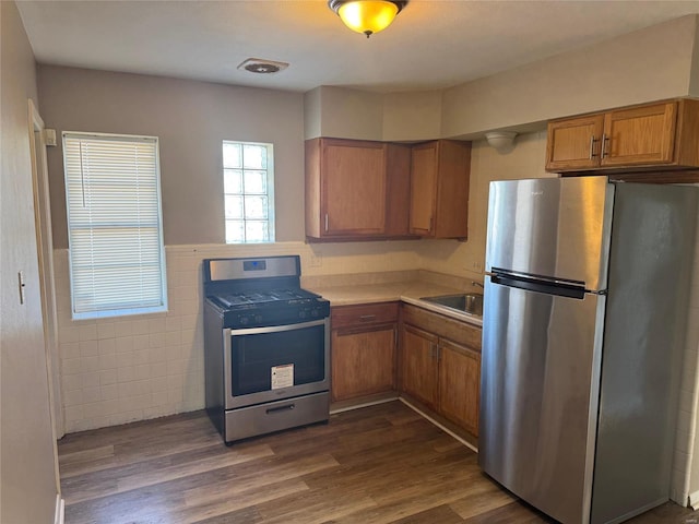 kitchen featuring dark wood-style floors, light countertops, appliances with stainless steel finishes, brown cabinetry, and a sink