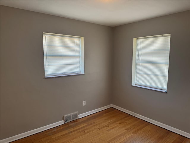 unfurnished room featuring a healthy amount of sunlight, visible vents, light wood finished floors, and baseboards