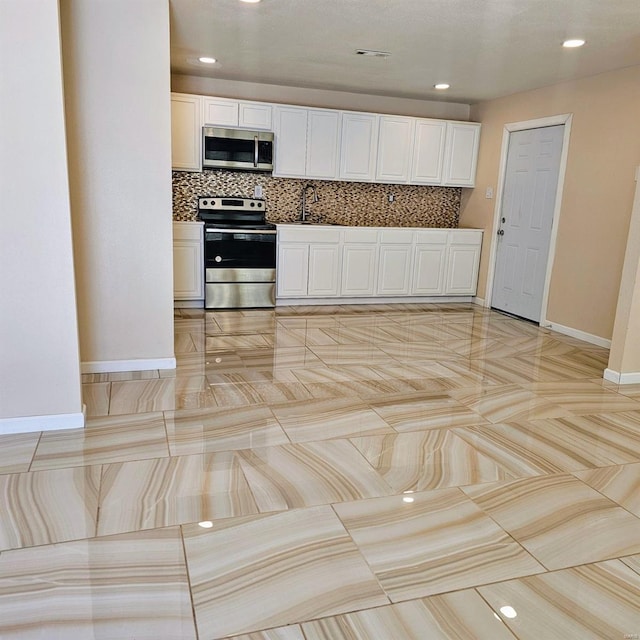 kitchen featuring appliances with stainless steel finishes, white cabinetry, backsplash, and baseboards